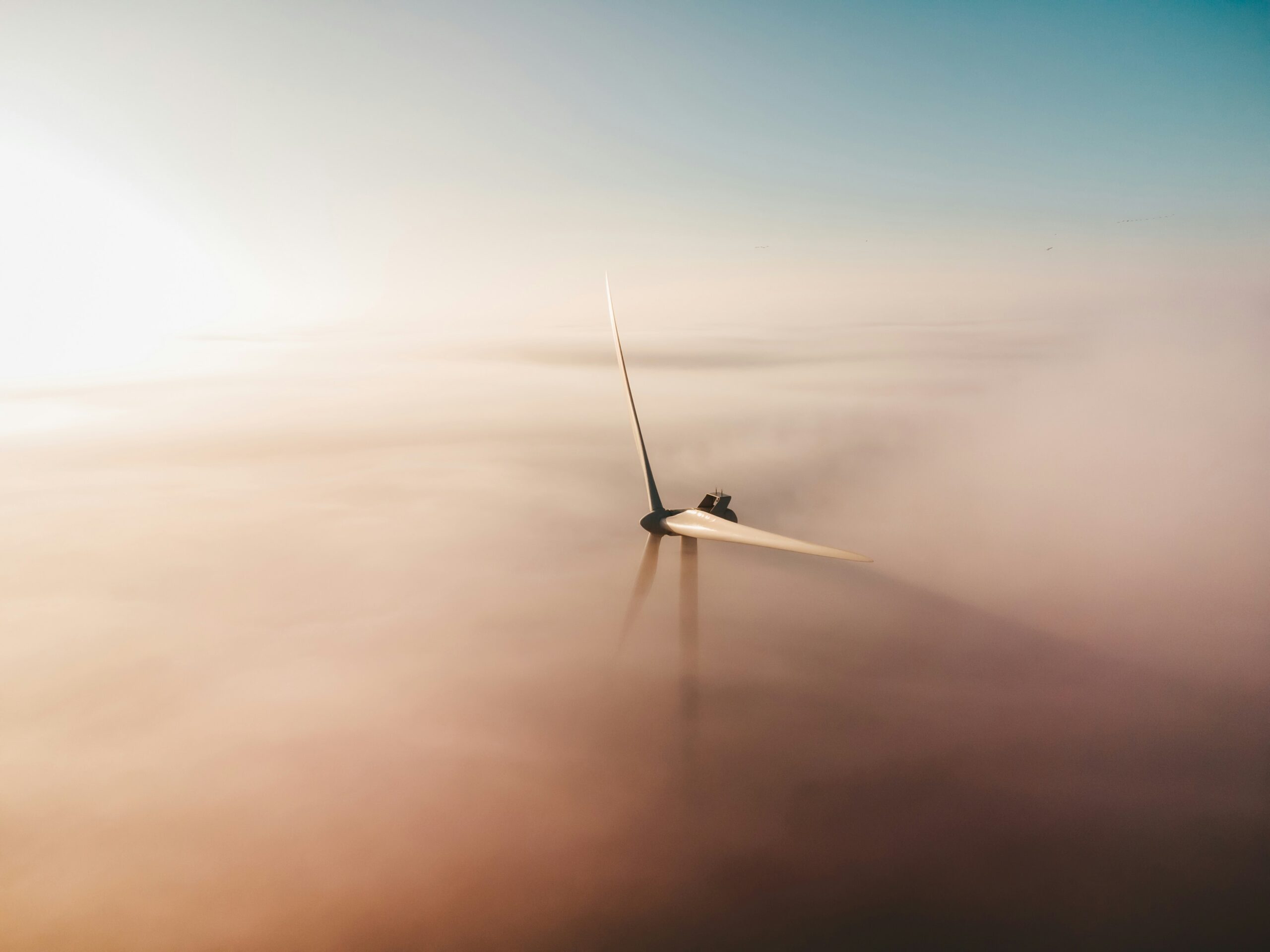 Man sieht die Rotorenblätter eines Windrades aus der Vogelsperspektive zwischen den Wolken.