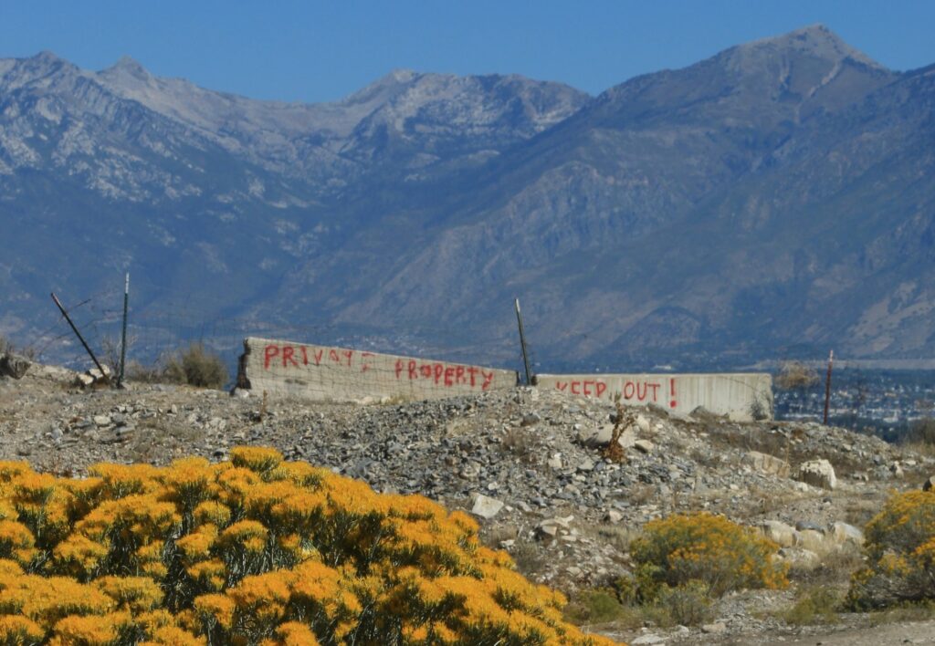 Eine bergige, steppenhafte Landschaft. Vor der Gebirgskulisse steht auf einer Ebene ein an beiden Seiten abgebrochener Mauerrest. Darauf wurde mit Sprühfarbe geschrieben: Private property, keep out.