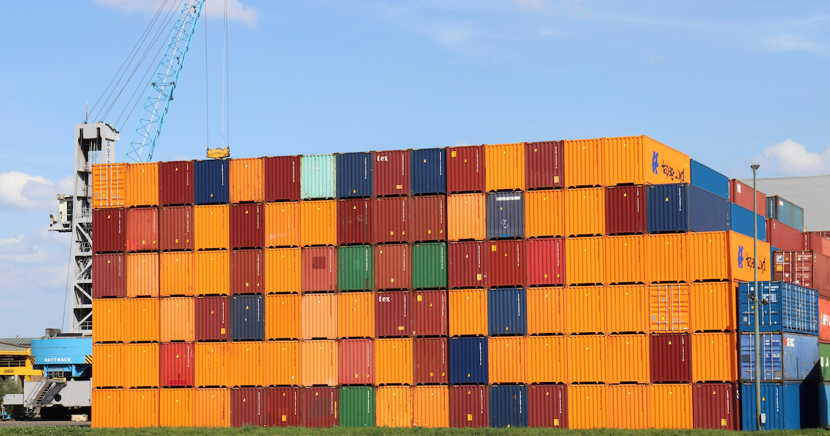 Ein großer Stapel von Schiffscontainern, im Hintergrund ein Kran.